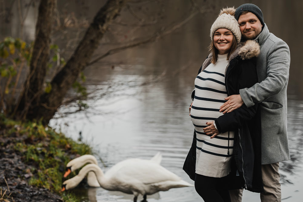 Schwangere mit Partner und Schwaenen am Weiher