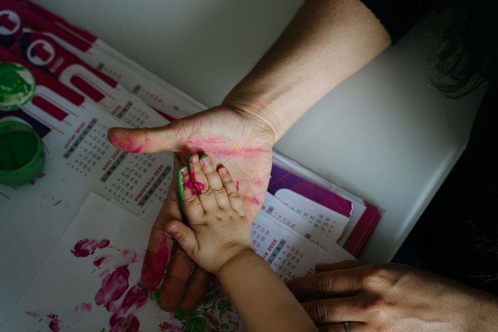 Kinderhand in Erwachsenenhand mit Fingerfarbe bei dokumentarischer Familienfotografie