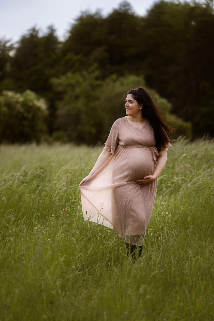 Schwangere läuft über ein Feld und schaut seitlich, während sie auf Fotograf zuläuft
