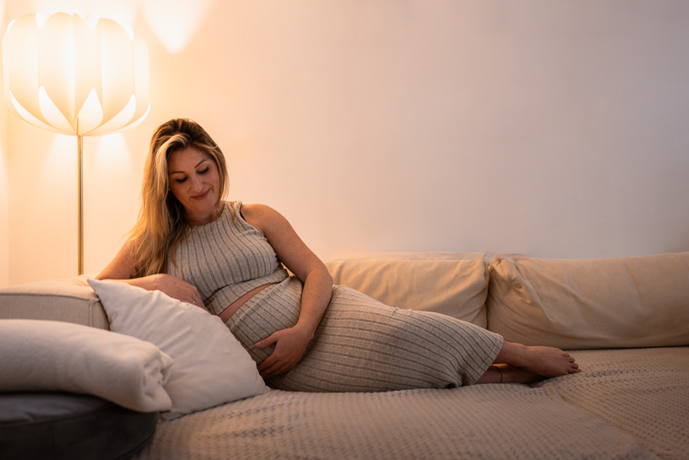 Schwangere Frau bei Babybauchshooting zu Hause auf dem Sofa. Fotograf kommt im Saarland nach Hause